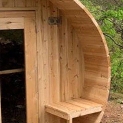 Wooden barrel-shaped sauna in a forest setting with trees and water in the background